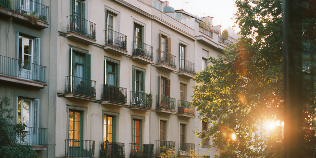 comunidades fachada de edificio de apartamentos con balcones y persianas verdes. la luz del sol brilla intensamente a través de árboles.