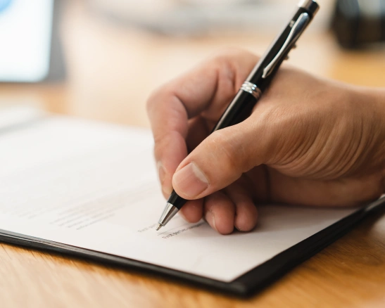 primer plano de una mano firmando un documento con un bolígrafo