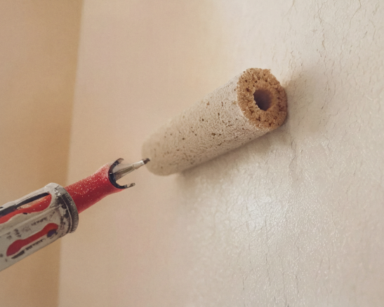 rodillo con textura de esponja y mango rojo aplicando pintura clara sobre una pared agrietada y texturizada.