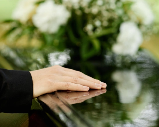 una mano de mujer sobre un ataúd negro con flores blancas